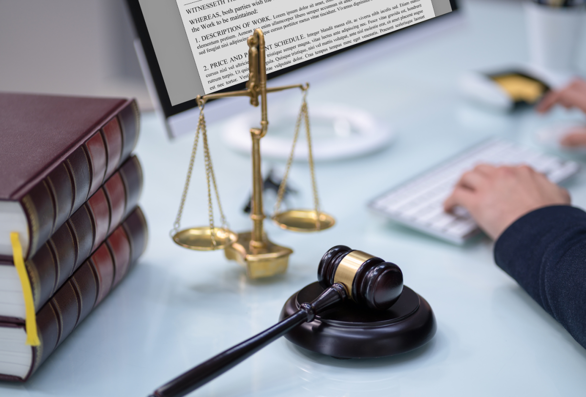 Im Fokus des Bildes ist ein Richterhammer, der auf einem Tisch liegt, dahinter steht eine Richterwaage und am linken Rand des Bildes liegt ein Stapel von drei Büchern.